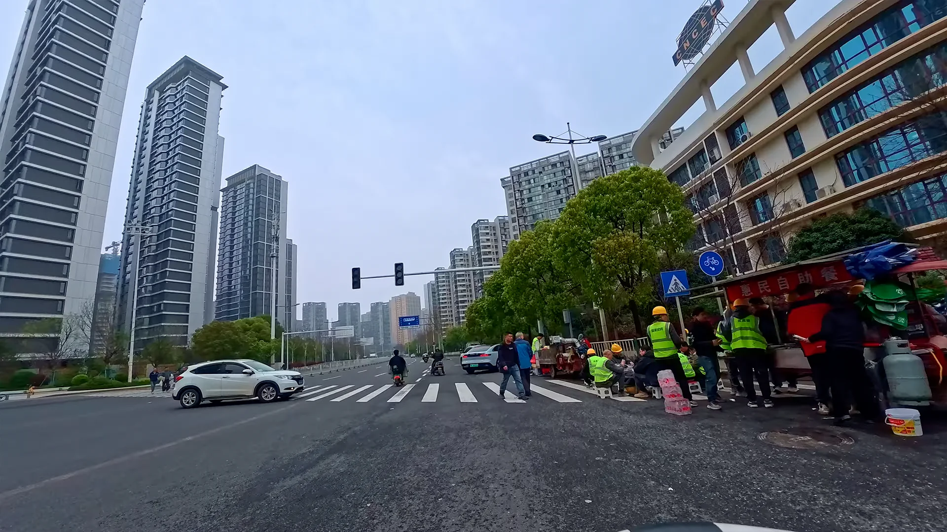 Changsha street intersection showing everyday urban life with pedestrians, workers and electric scooters under an overcast sky