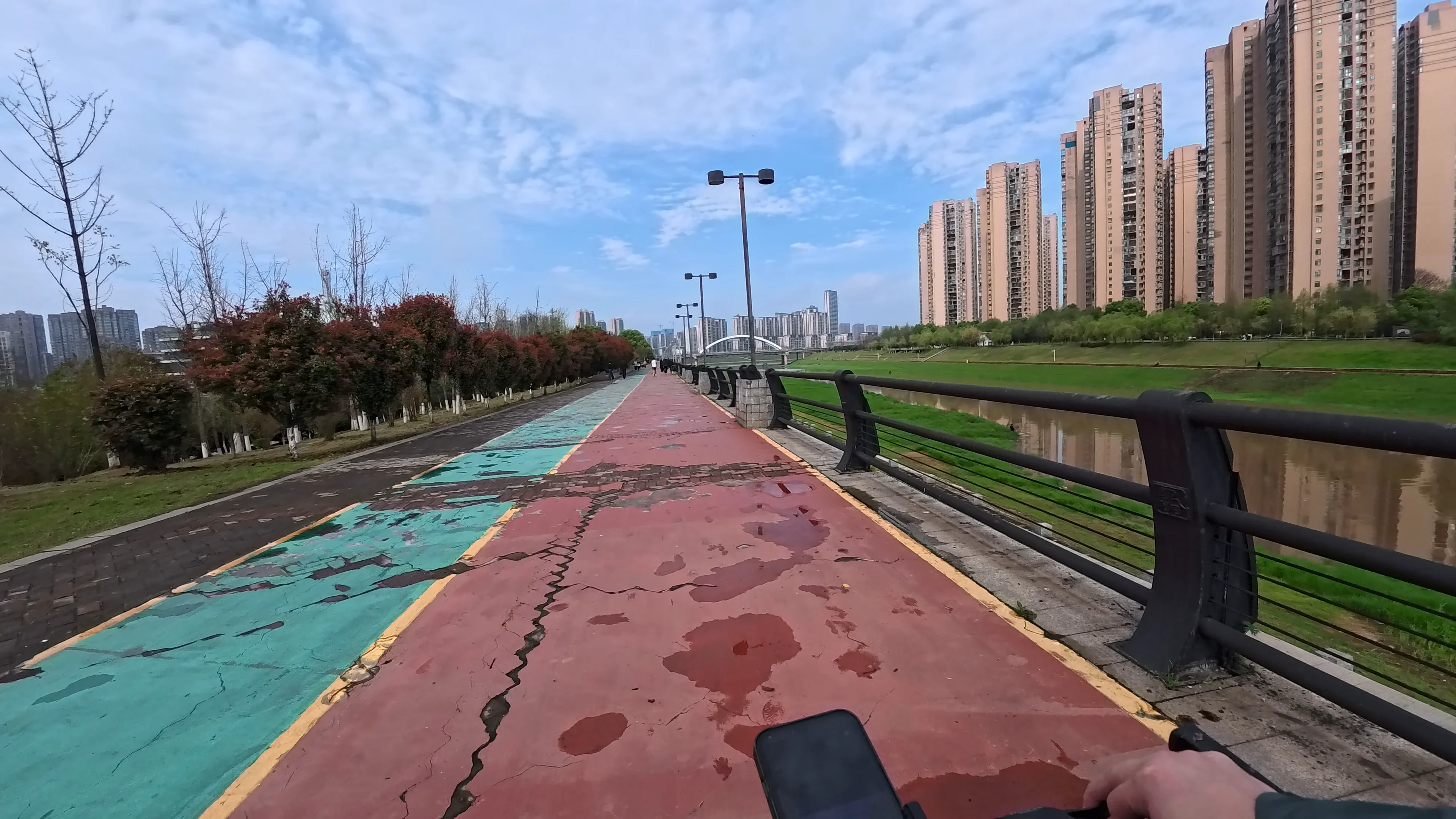 POV cycling along a colorful riverside bike path beside modern residential towers in Changsha, China after light rain